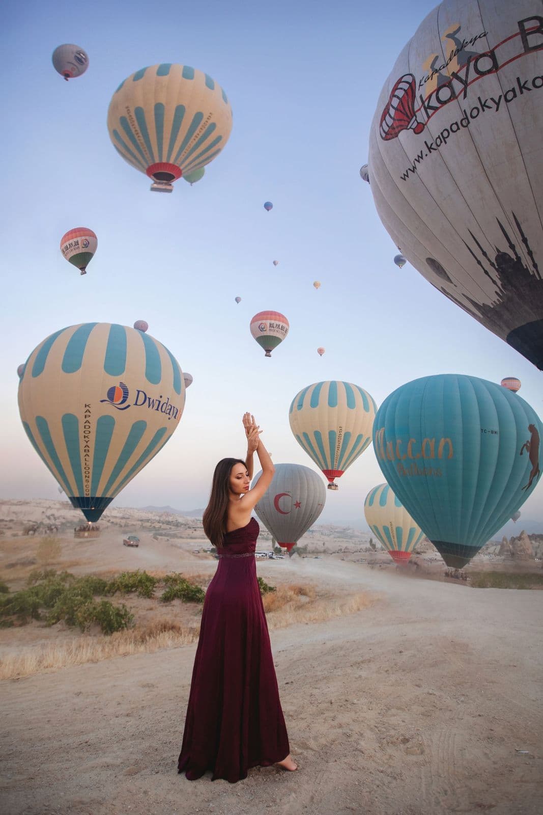 A woman in a red dress with balloons at sunrise