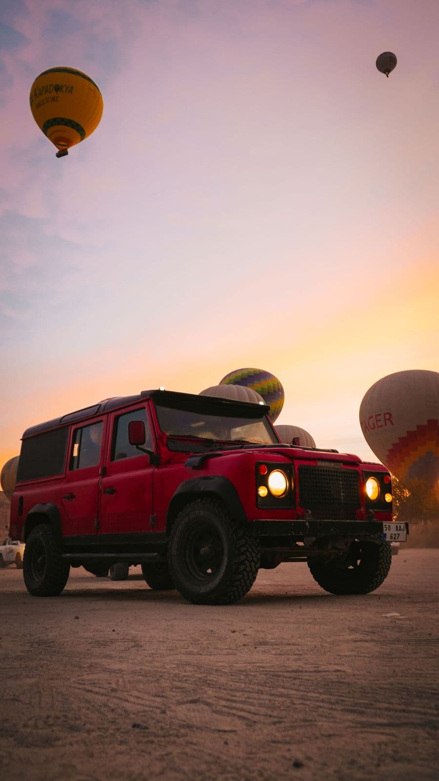 A jeep under hot air balloons at sunrise