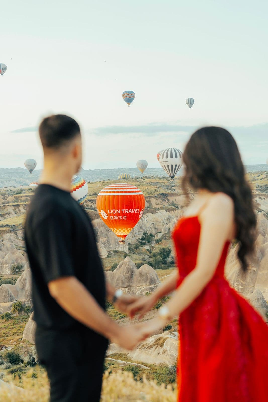 A couple holding hands while hot air balloons rise over Cappadocia